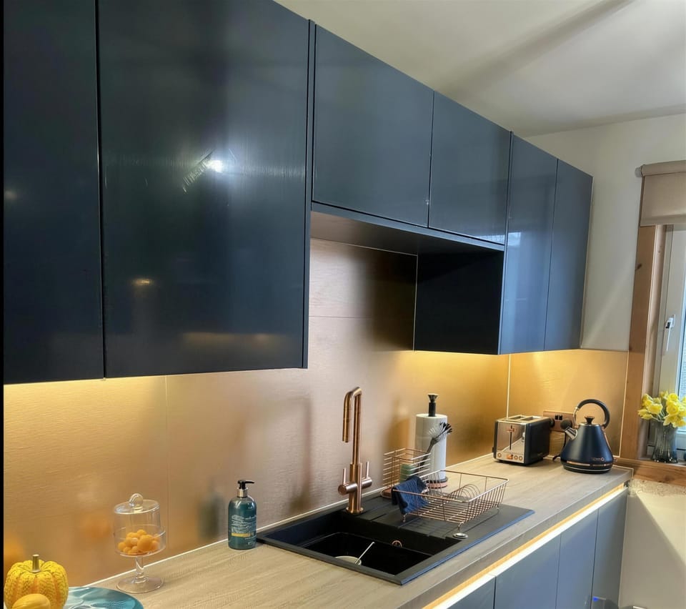 A kitchen with LED strip lighting under the wall cabinets and along the worktop, lighting a brushed copper splashback